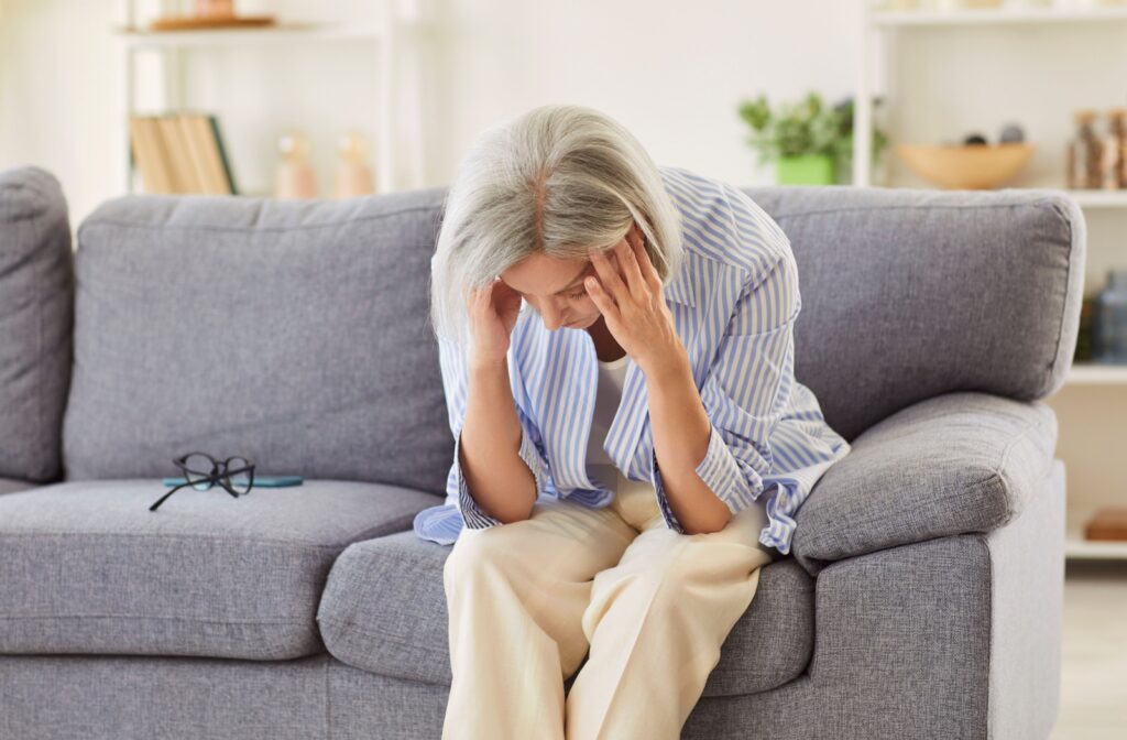 An adult sits on a couch, head in their hands, exhausted from caregiving for a senior parent without time for themself.