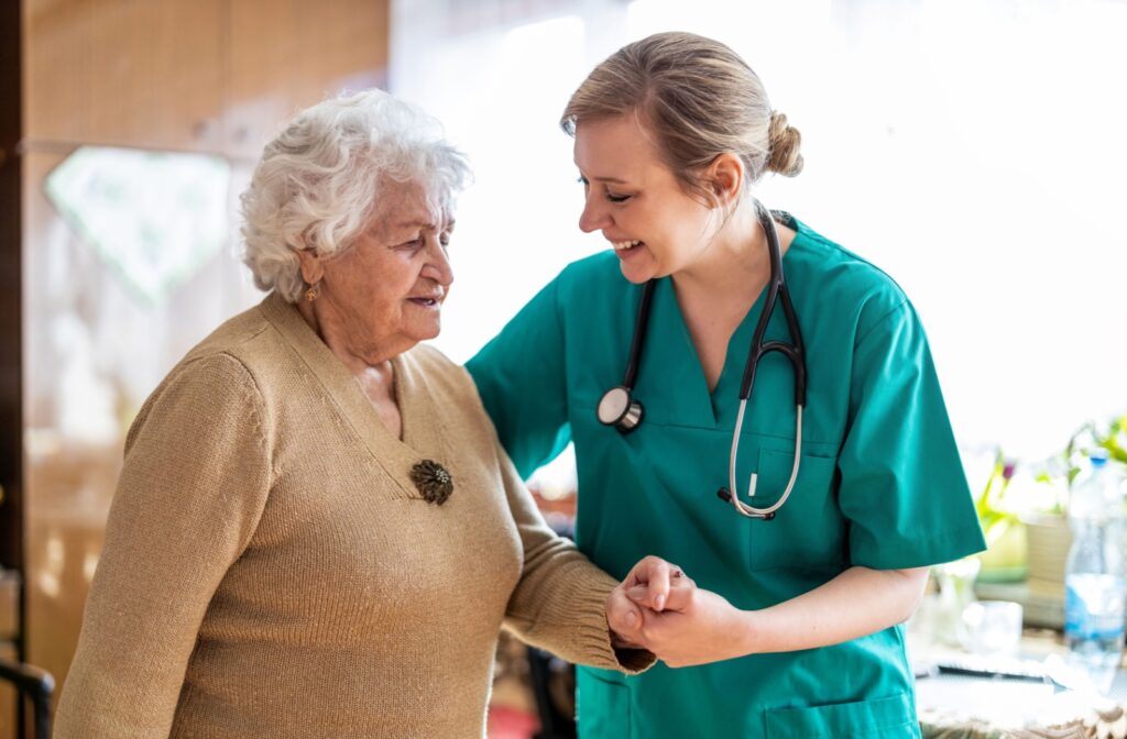 A happy nurse holds a senior’s hand while providing assistance in an assisted living community