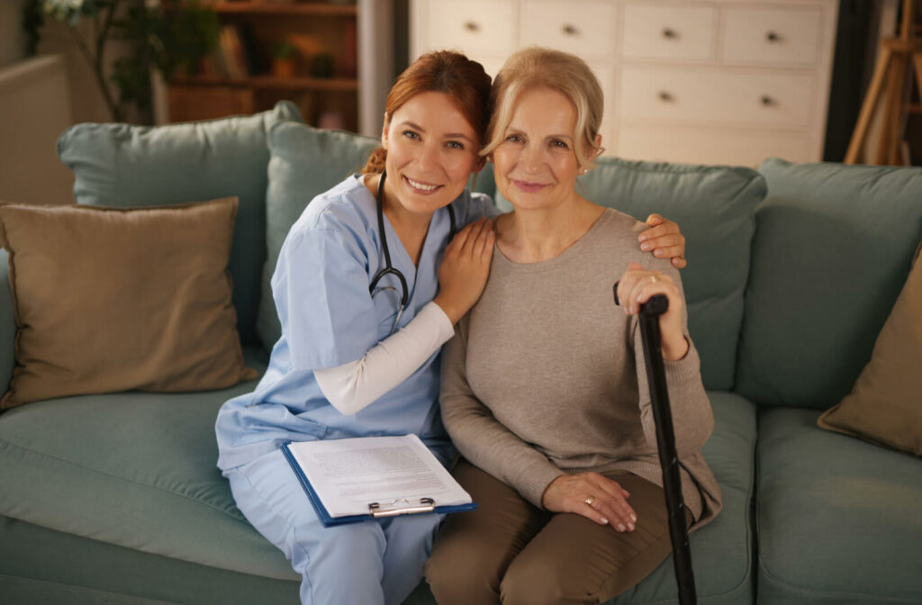 A nurse with their arms around the shoulders of a smiling resident on a couch in respite care