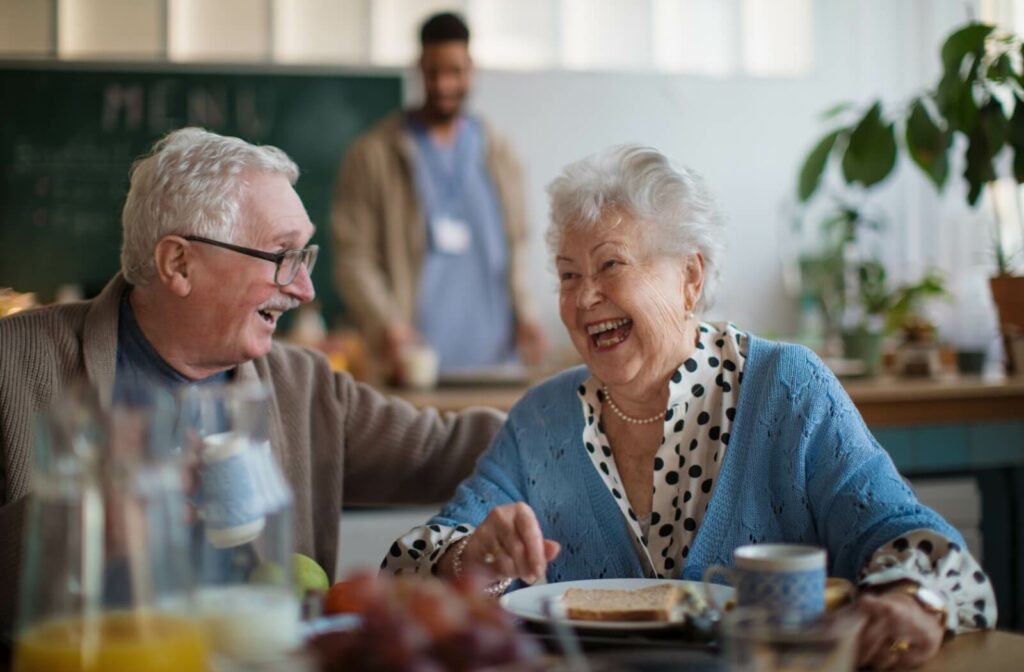 a senior couple laugh as they share a meal together at a senior living community.