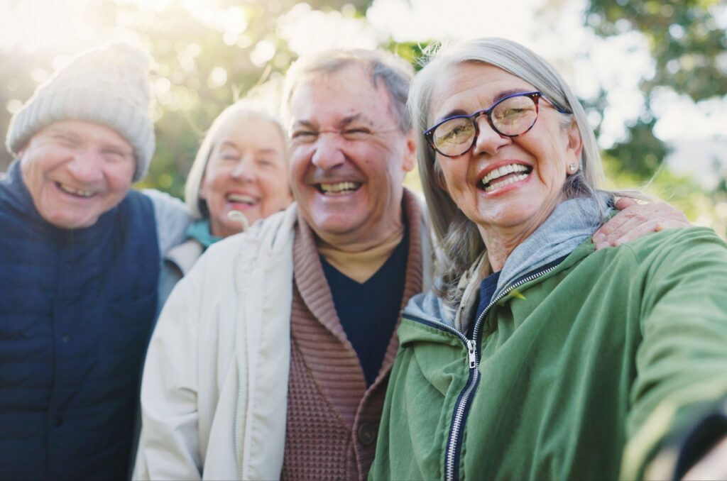 A group of senior friends smile and embraces while outside on a brisk fall day
